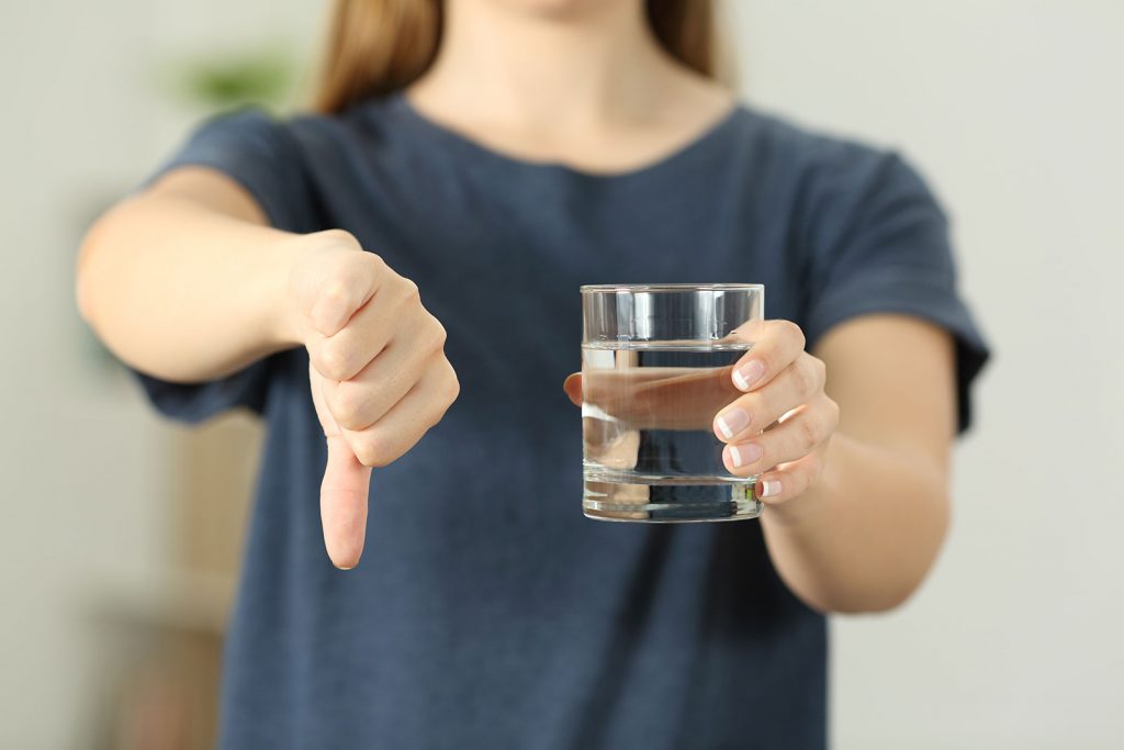 Girl holding glass of water gives thumbs down.