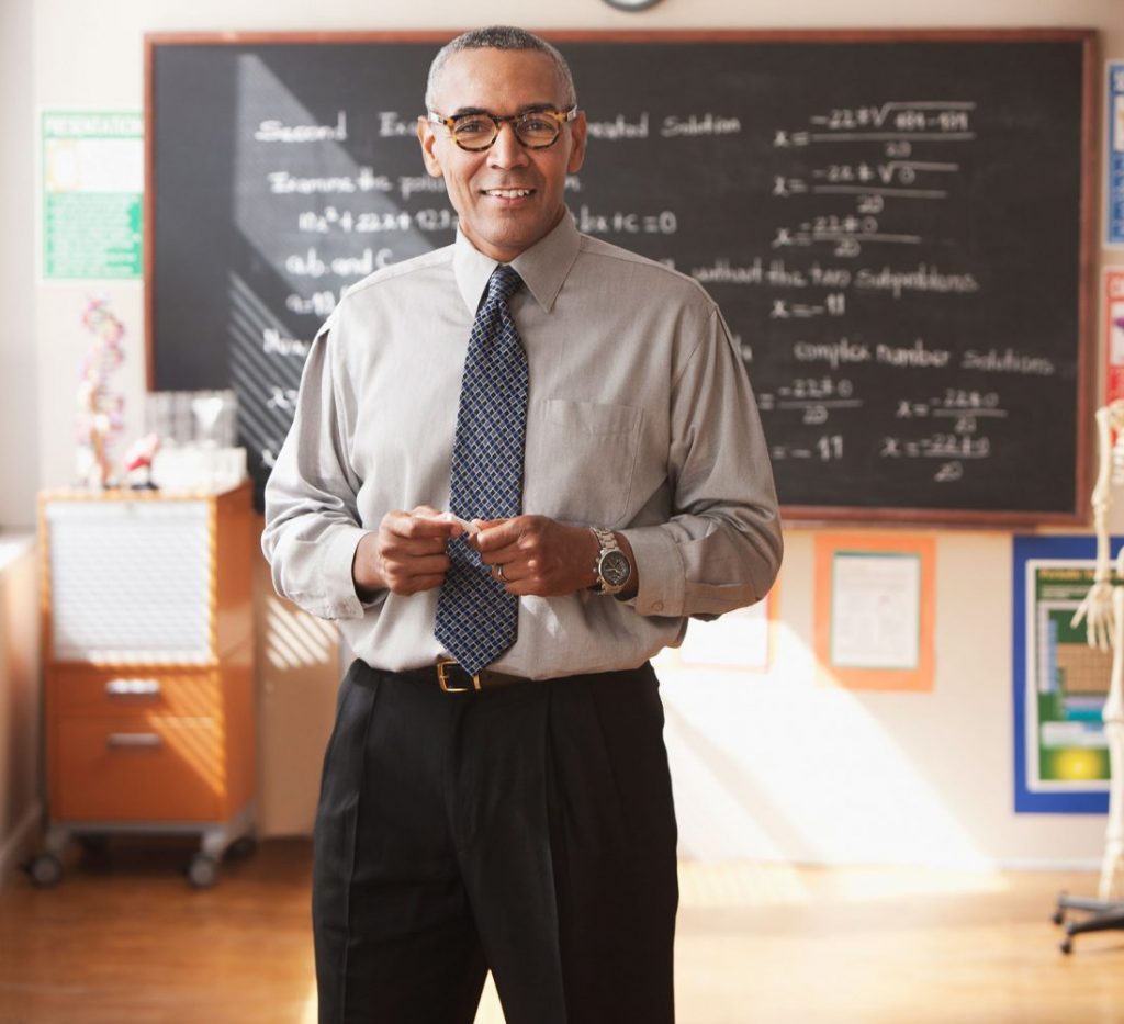 A teacher in a classroom with a blackboard behind him.