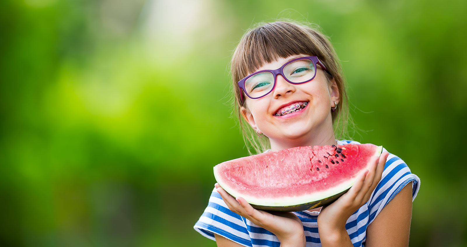 Young girl with glasses eating watermelon.
