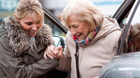 Young woman helps senior woman out of car