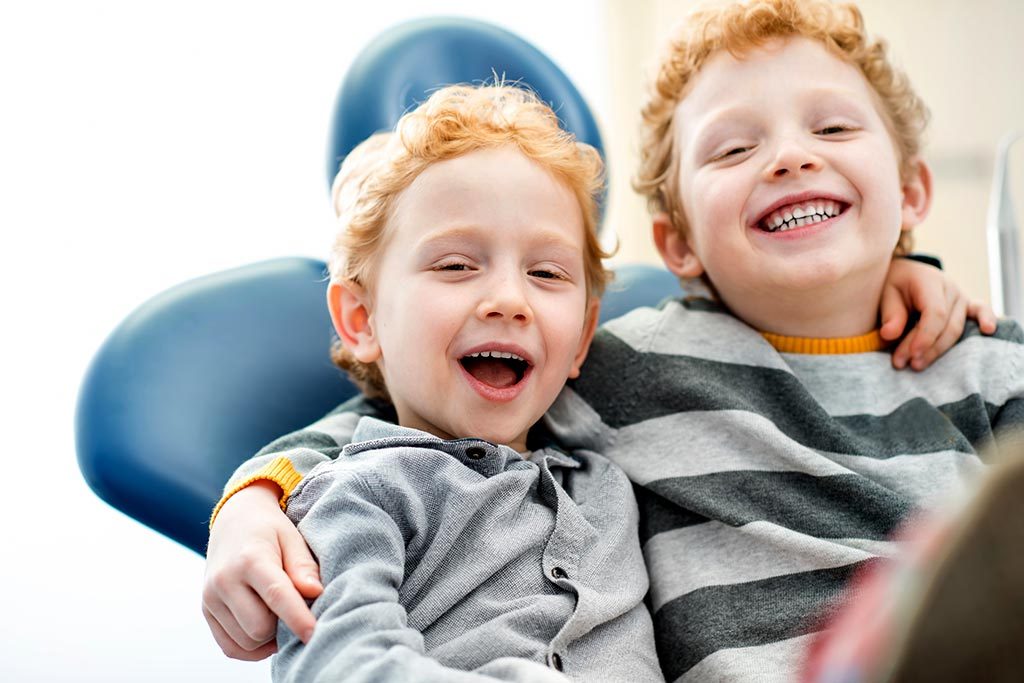 Two young boys smile while sitting in a dental chair.