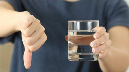 Holding a glass of water and pointing a thumb down to indicate that the water is not safe to drink.