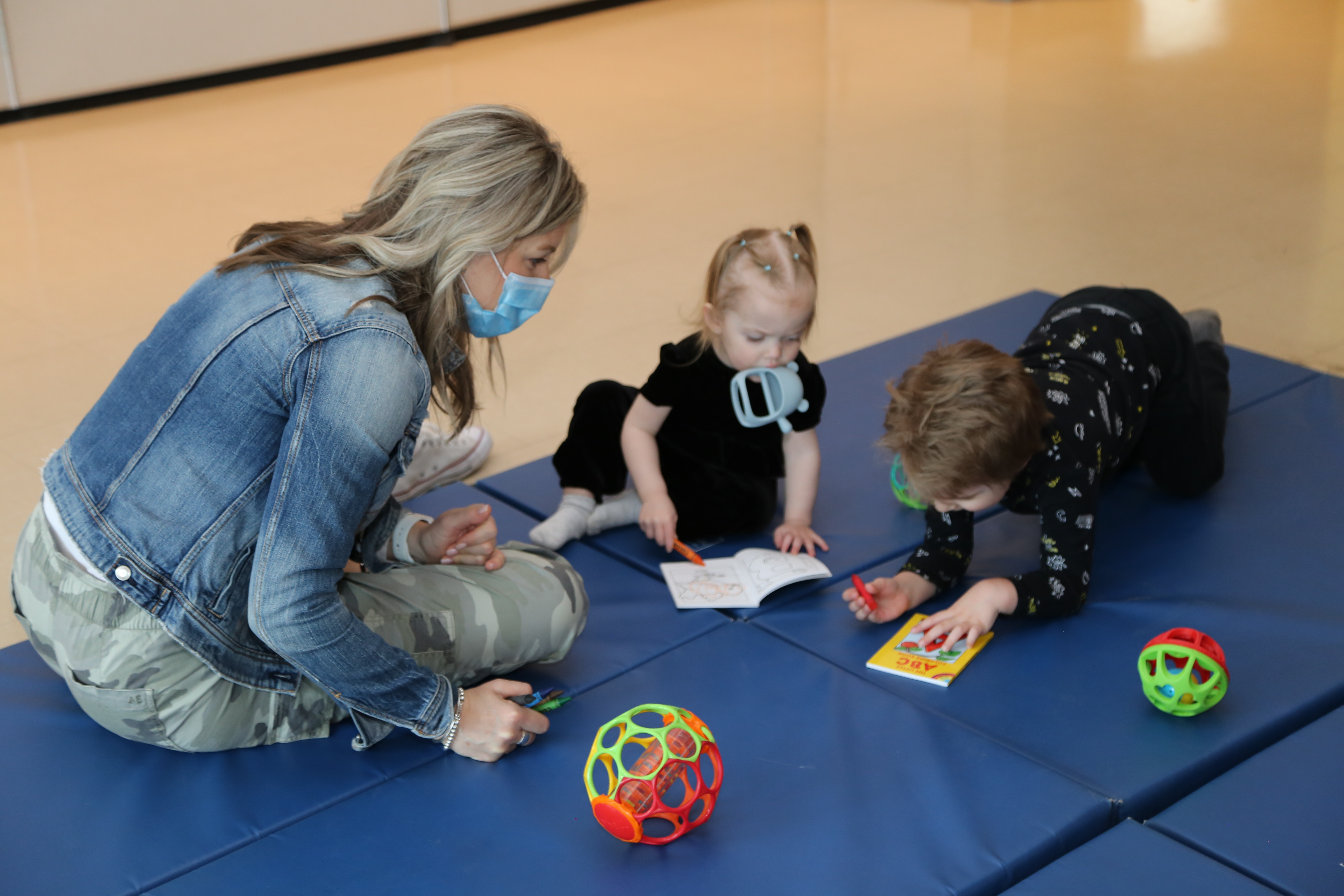A Public Health Nurse with babies on a mat playing with toys at a drop-in class.