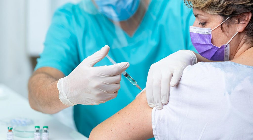 A woman wearing a mask receives a flu vaccine in her arm.