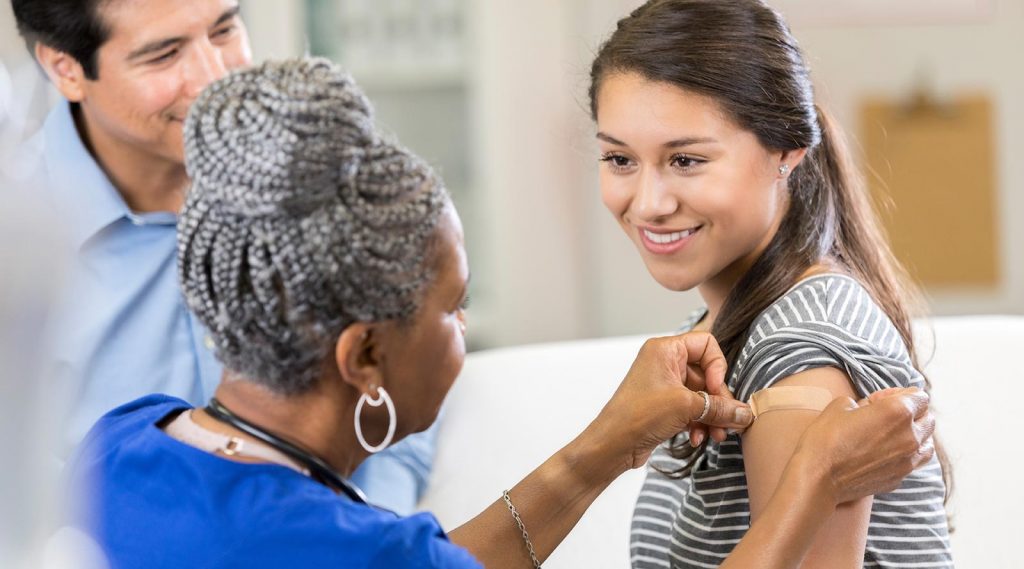 A nurse applies a bandage to the arm of a teen after receiving a vaccine.