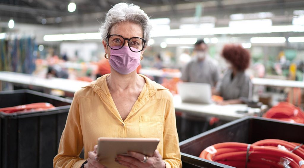 An elderly woman wearing a mask while working in a factory.