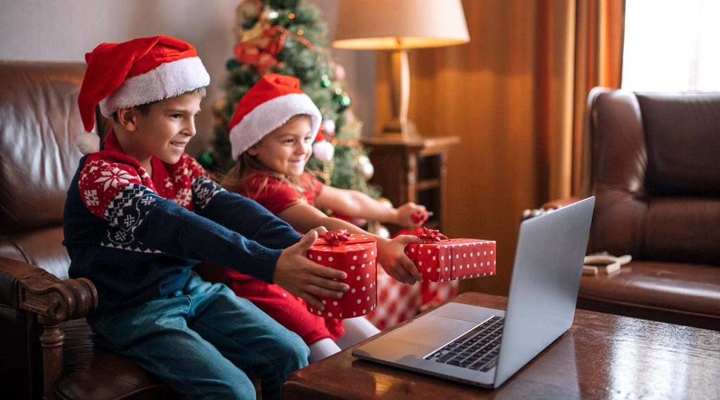 Two children hold up Christmas gifts in front of a laptop.