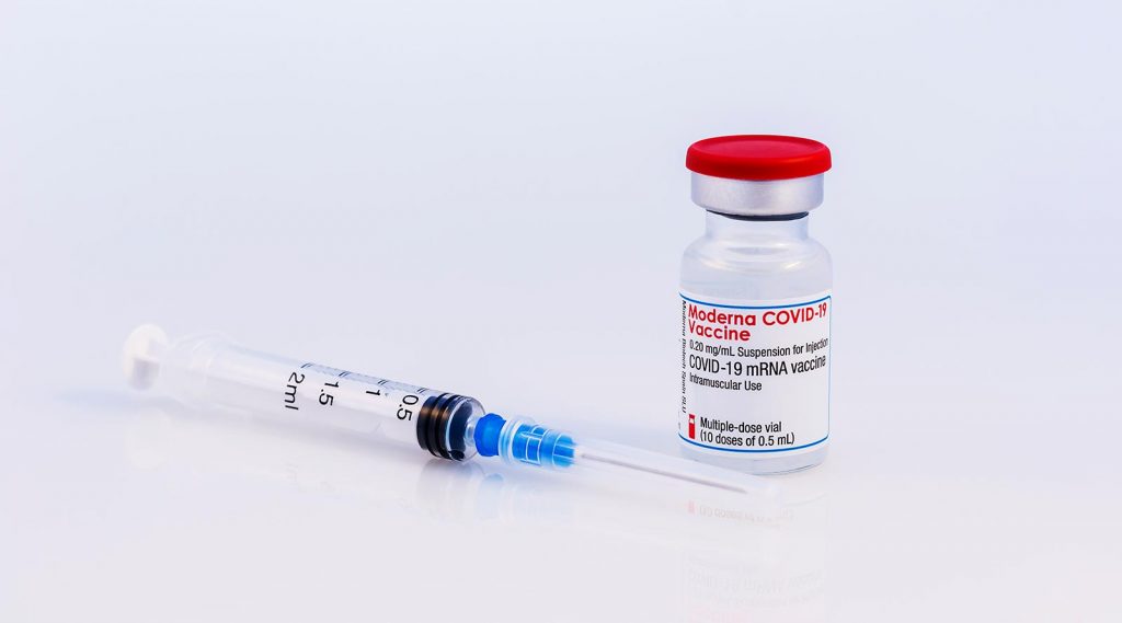 A vial of the Moderna COVID-19 vaccine and a syringe.