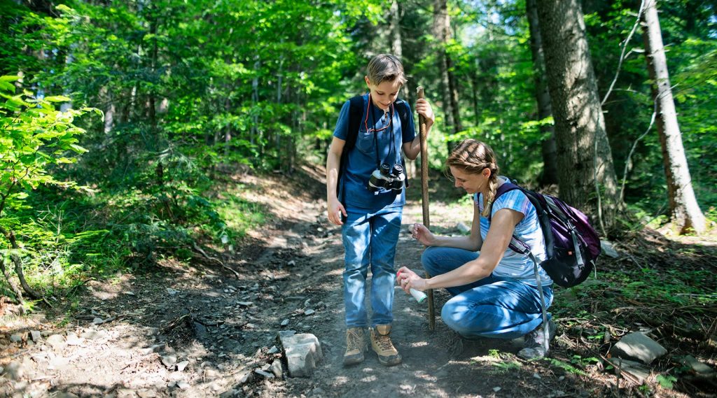 A mother spraying her son with tick repellant before they go on hike through the forest.