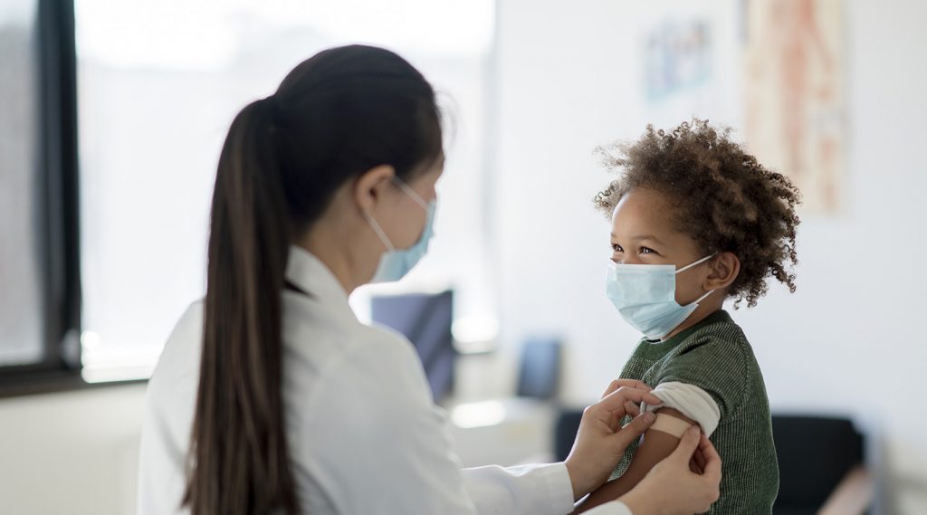 A nurse putting a band-aid on a child after receiving a covid-19 vaccine.