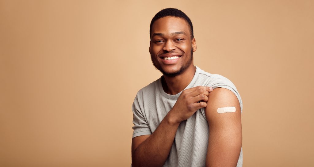 Portrait Of Happy Vaccinated African Man Showing His Arm After Coronavirus Antiviral Vaccine Shot.