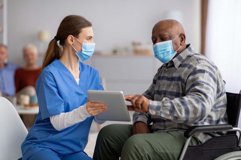 Female nurse helping senior man in wheelchair using digital tablet.