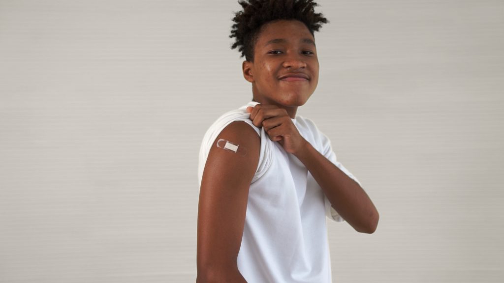 African American teenager showing COVID-19 vaccine bandage merrily in concept of coronavirus vaccination program to vaccinate citizen .