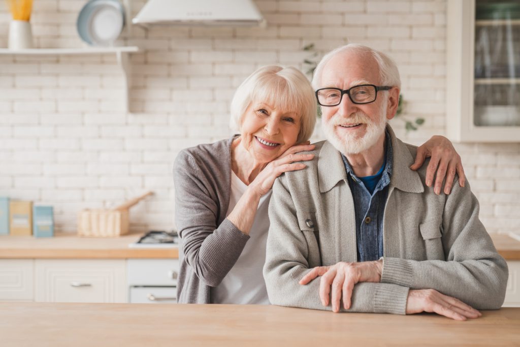 An elderly couple embrace in the kitchen of their home