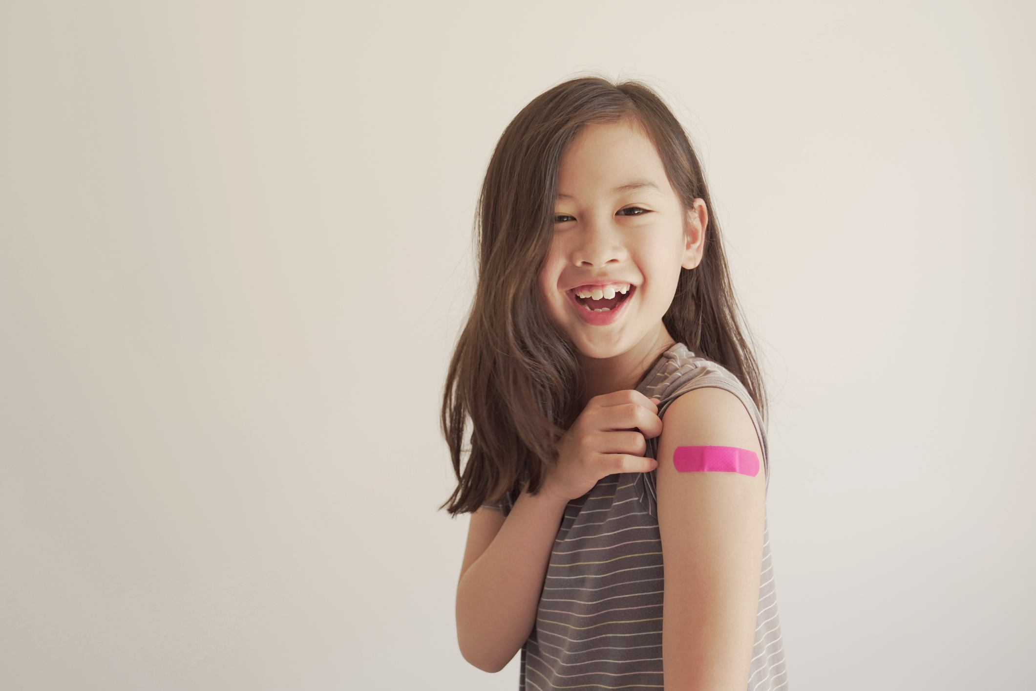 Mixed Asian young girl showing her arm with pink bandage after being vaccinated.