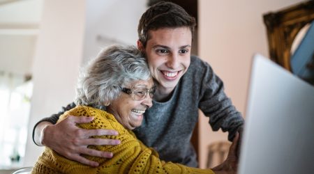 Grandson and grandmother embracing and using laptop at home