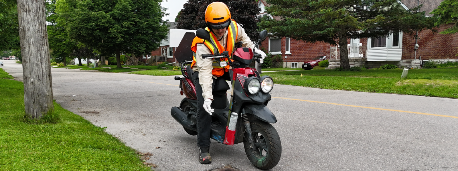 Technician applying larvicide by hand to roadside catch basins while on a motorized scooter.