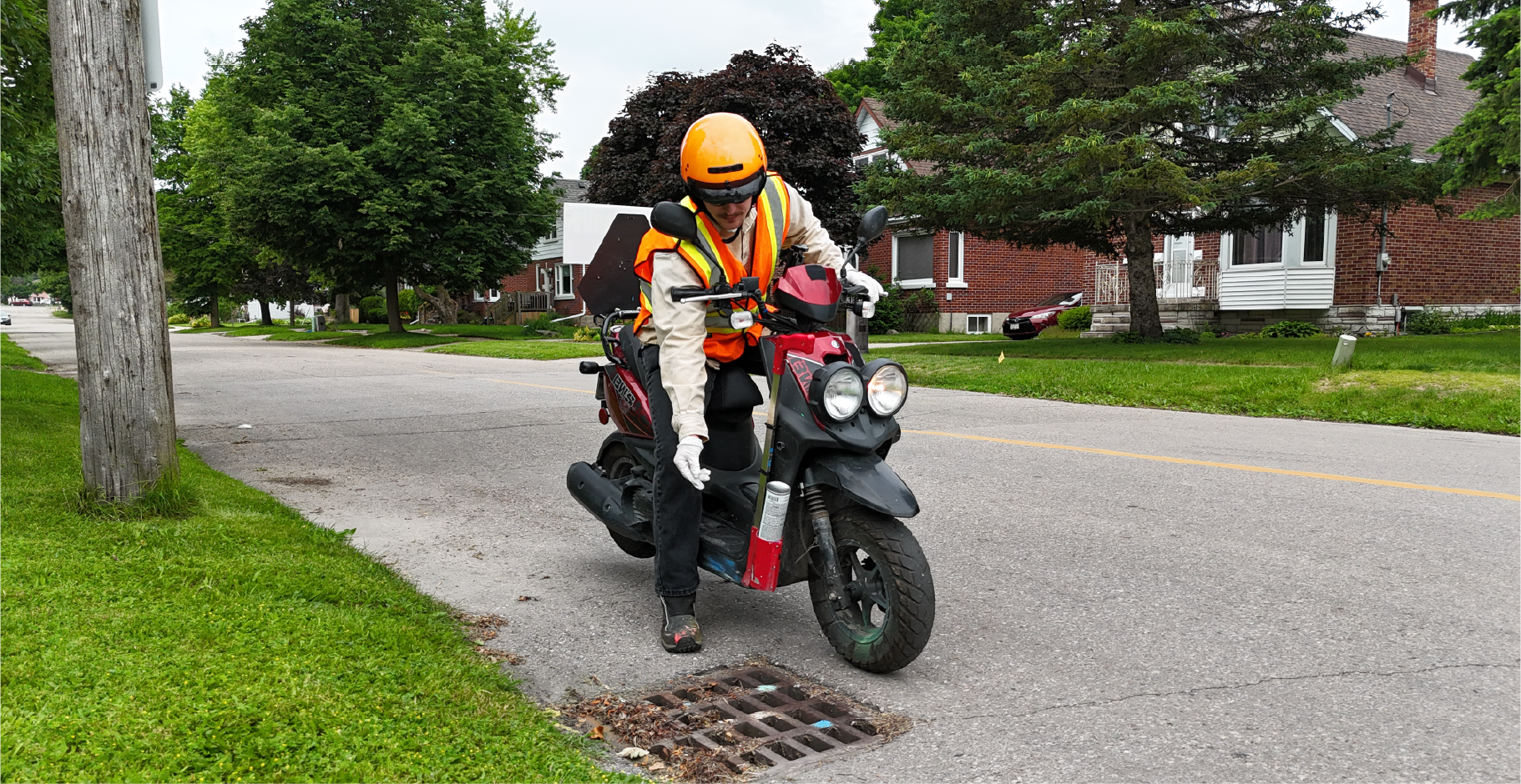 Technician applying larvicide by hand to roadside catch basins while on a motorized scooter.